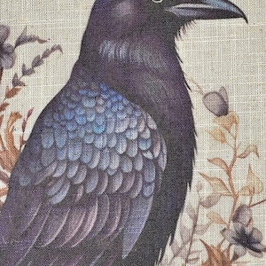 May include: A black raven with iridescent blue feathers is perched on a branch with brown and white flowers. The raven's eye is visible and the background is a beige linen fabric.