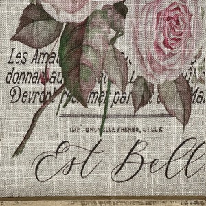 Pu&ograve; includere: Una stampa in stile vintage su tessuto di juta con un bouquet di rose rosa con foglie verdi. Il testo "Les Ama donnan au Devrdol te met par IMF. GRUYELLE FRERES, LILLE Ma Est Bell" &egrave; stampato sul tessuto.