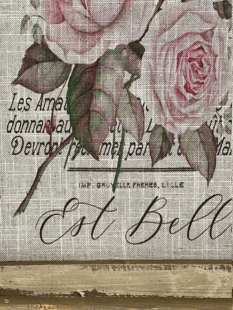 Pu&ograve; includere: Una stampa in stile vintage su tessuto di juta con un bouquet di rose rosa con foglie verdi. Il testo "Les Ama donnan au Devrdol te met par IMF. GRUYELLE FRERES, LILLE Ma Est Bell" &egrave; stampato sul tessuto.