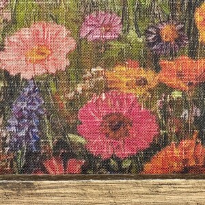 May include: A close-up of a floral print featuring a variety of colorful flowers, including pink, red, orange, and purple blooms. The flowers are set against a green background, with a wooden frame at the bottom.