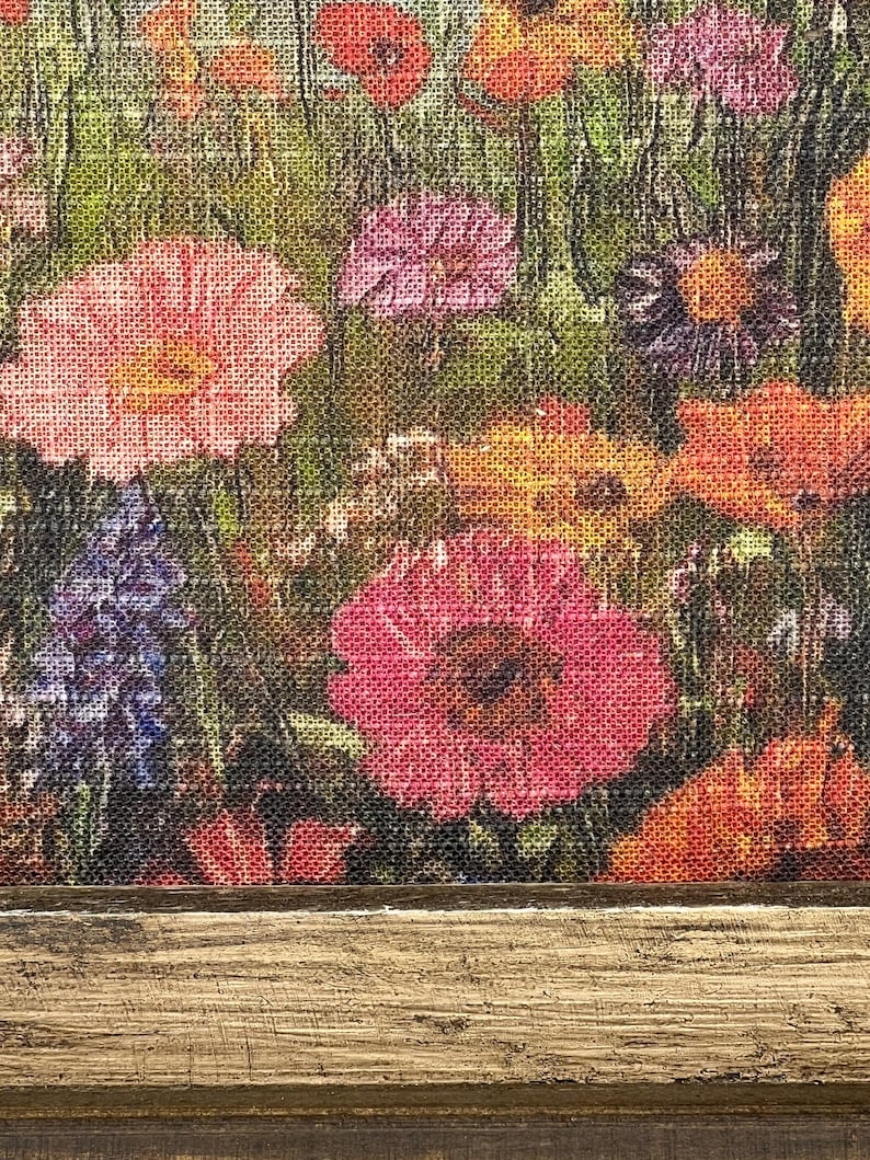 May include: A close-up of a floral print featuring a variety of colorful flowers, including pink, red, orange, and purple blooms. The flowers are set against a green background, with a wooden frame at the bottom.