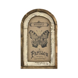 May include: A framed burlap print with a vintage butterfly illustration and the text "Butterfly Le Papillon (The Butterfly)". The frame is a distressed white and brown wood with an arched top.