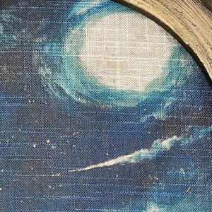 May include: A close-up of a blue and white abstract painting on a textured canvas. The painting features a large white circle surrounded by blue and white brushstrokes.