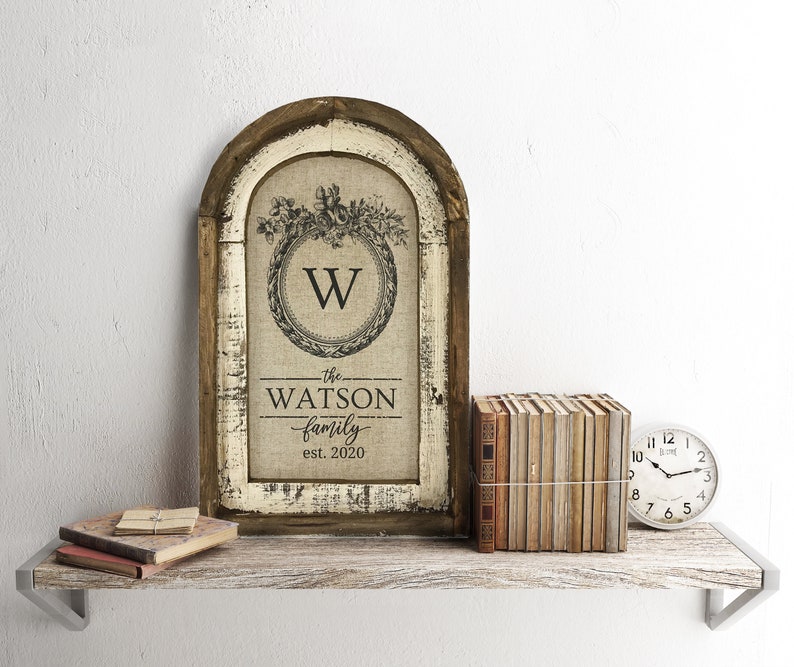 May include: A rustic wooden framed sign with a burlap background featuring a wreath with the letter "W" in the center. The text "the WATSON family est. 2020" is printed below the wreath.