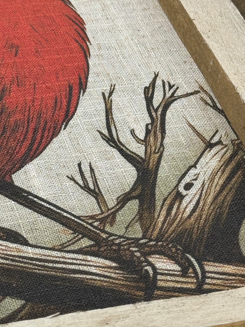 May include: A close-up of a red bird perched on a branch. The bird is depicted in a stylized, almost cartoon-like manner, with a thick, rounded body and a short, stubby beak. The branch is brown and gnarled, with a few smaller branches extending from it. The background is a light beige, suggesting a canvas or fabric surface.