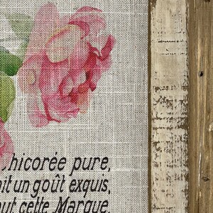 May include: A burlap fabric with a pink rose and green leaves printed on it. The fabric has the text "chicor&eacute;e pure,  it un go&ucirc;t exquis,  ut cette Marque." printed on it.