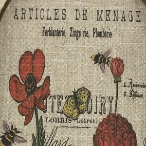 May include: A vintage-style print with the text "ARTICLES DE MENAGE Ferblanterie, Zingu rie, Plomberie" and a floral design featuring red poppies, a yellow butterfly, and black and yellow bees.