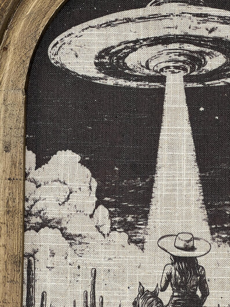 Puede incluir: Una ilustraci&oacute;n en blanco y negro de un OVNI sobrevolando un paisaje des&eacute;rtico con un vaquero o una vaquera montando a caballo en primer plano. El OVNI emite un rayo de luz.