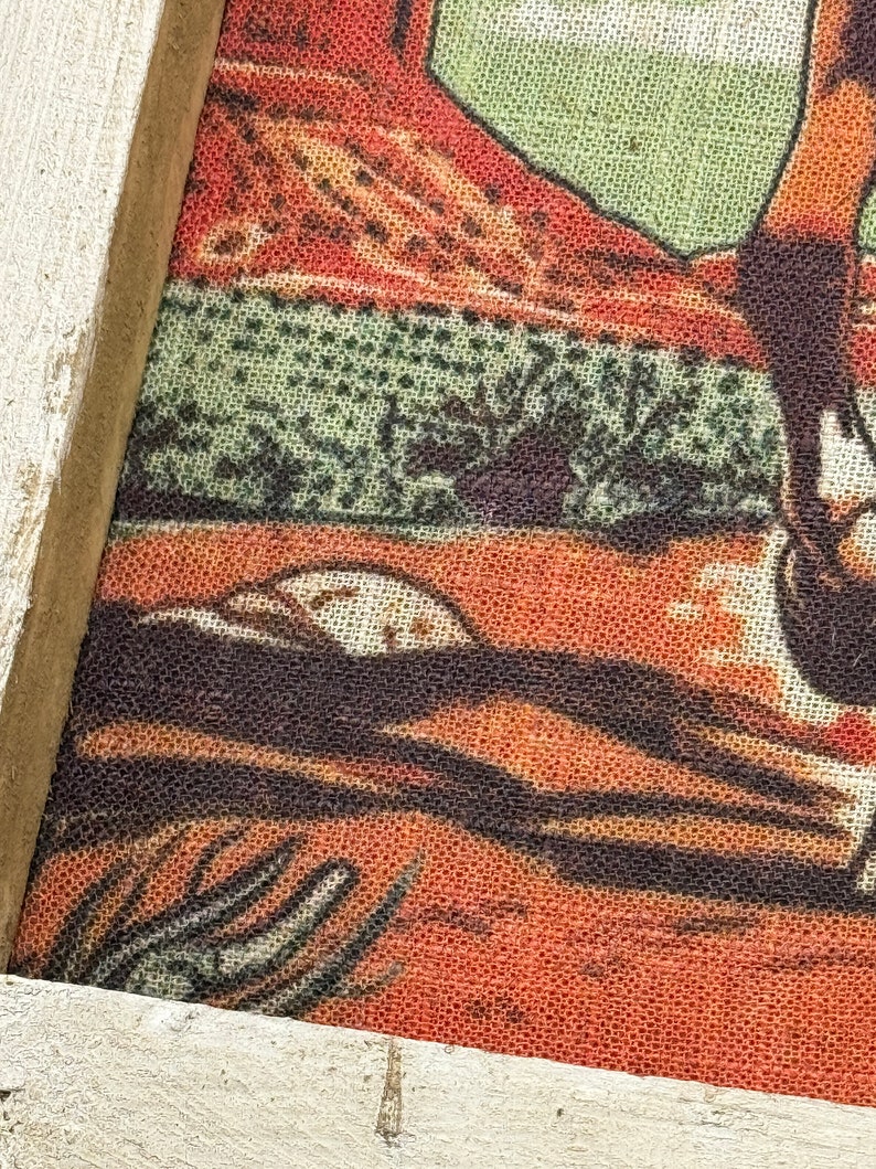 May include: A framed piece of art with a red, green, and brown design. The art is printed on a textured fabric.