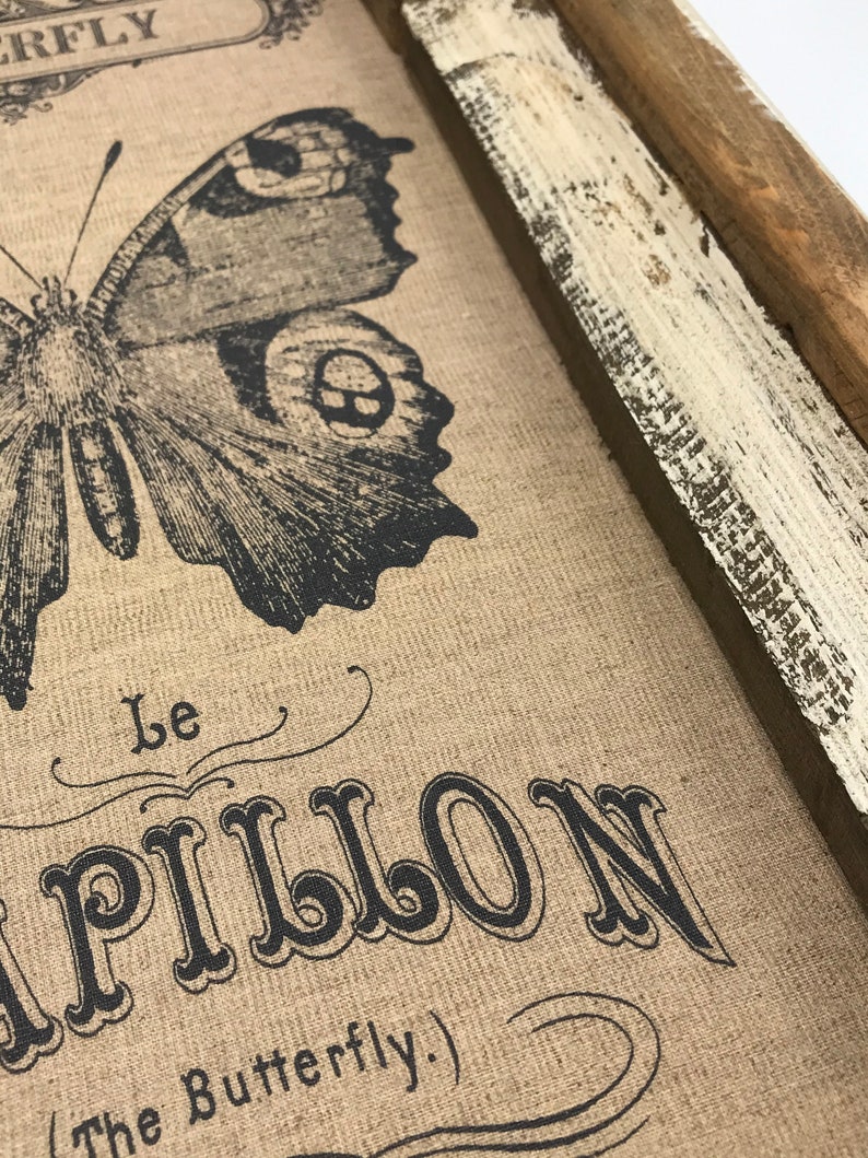 May include: A framed burlap print featuring a black and white butterfly illustration. The text "Le Papillon (The Butterfly)" is printed below the butterfly.