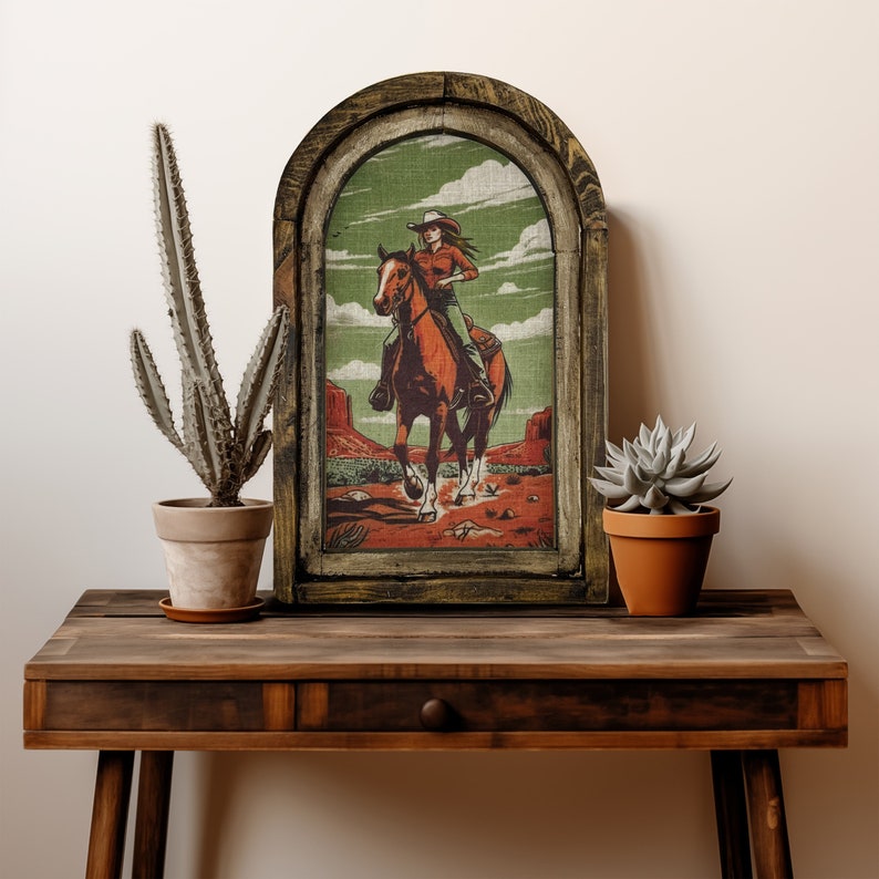 May include: A wooden framed wall decor with a vintage illustration of a woman riding a horse in a desert landscape. The frame has a dark brown finish and the illustration is printed on a canvas.
