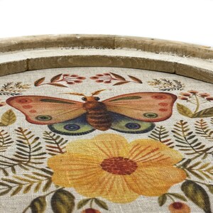 May include: A round wooden tray with a linen fabric insert featuring a floral design with a butterfly and yellow flower. The tray is perfect for serving snacks or drinks.