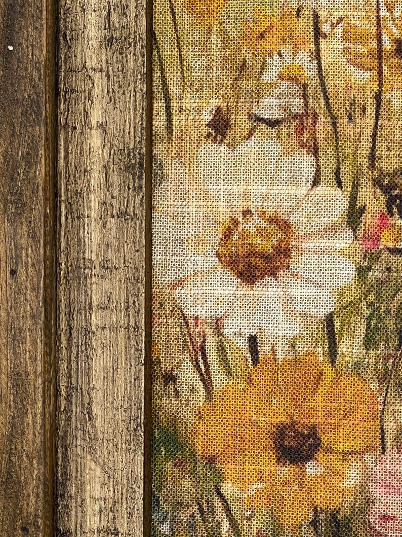 Puede incluir: Una impresi&oacute;n sobre lienzo enmarcada con un dise&ntilde;o floral que presenta flores blancas y amarillas sobre un fondo de arpillera. El marco est&aacute; hecho de madera con un acabado r&uacute;stico.