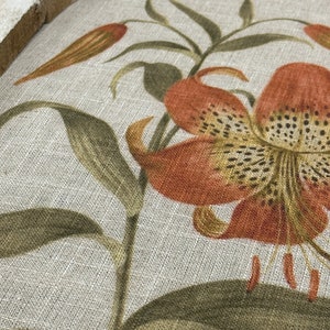 Peut inclure: Gros plan sur un tissu &agrave; motif floral. Le tissu pr&eacute;sente un grand lys orange avec des taches brunes et des feuilles vertes. Le tissu a une texture de lin.