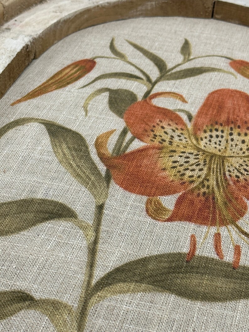 Peut inclure: Gros plan sur un tissu &agrave; motif floral. Le tissu pr&eacute;sente un grand lys orange avec des taches brunes et des feuilles vertes. Le tissu a une texture de lin.