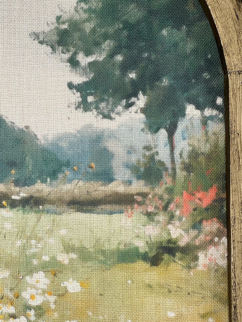 May include: A landscape painting featuring a field of wildflowers and a large tree. The artwork uses a palette of greens, yellows, and whites, with a hint of red flowers. The painting is framed in a gold-colored, arched wooden frame.