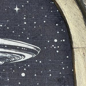 May include: A black and white illustration of a flying saucer against a dark blue background with white stars. The image is framed in a gold-painted wooden frame.