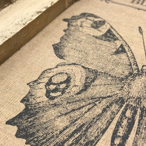 May include: Close-up of a brown burlap fabric with a black and white butterfly print. The butterfly has detailed wings and a textured body.