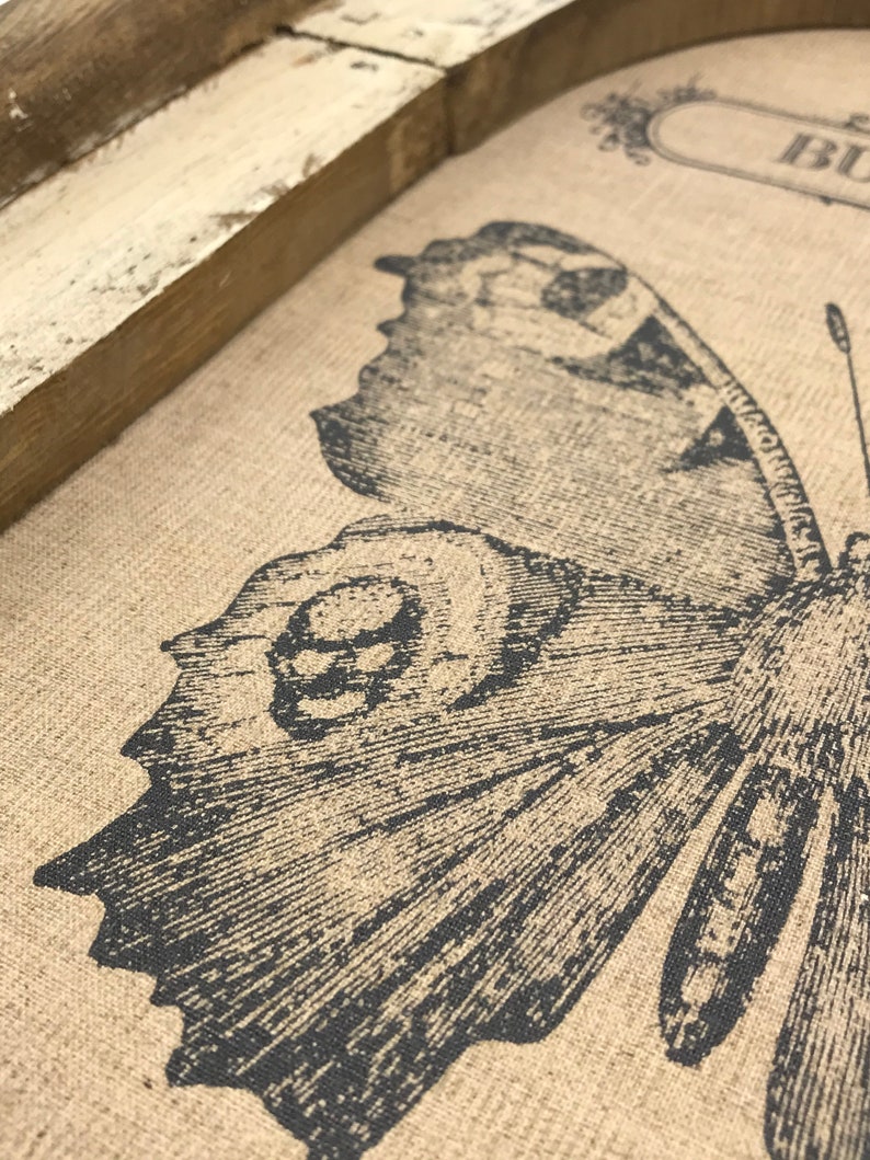 May include: Close-up of a brown burlap fabric with a black and white butterfly print. The butterfly has detailed wings and a textured body.