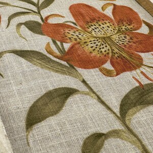 Peut inclure: Une impression sur toile encadr&eacute;e avec un motif floral mettant en vedette un grand lys orange avec des taches brunes sur un fond de lin beige.