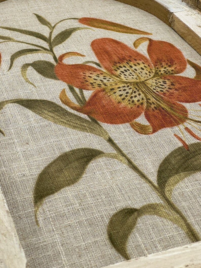 Peut inclure: Une impression sur toile encadr&eacute;e avec un motif floral mettant en vedette un grand lys orange avec des taches brunes sur un fond de lin beige.