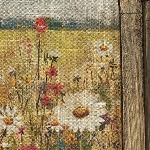 Puede incluir: Un primer plano de una impresi&oacute;n de lienzo enmarcada que representa un campo de flores silvestres. Las flores est&aacute;n pintadas en tonos de rojo, blanco y amarillo, y el fondo es de un verde suave. El lienzo es texturizado, lo que le da un aspecto r&uacute;stico.