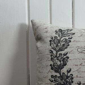 May include: A cream-colored pillow with a black floral design. The pillow has a textured fabric and a subtle sheen.