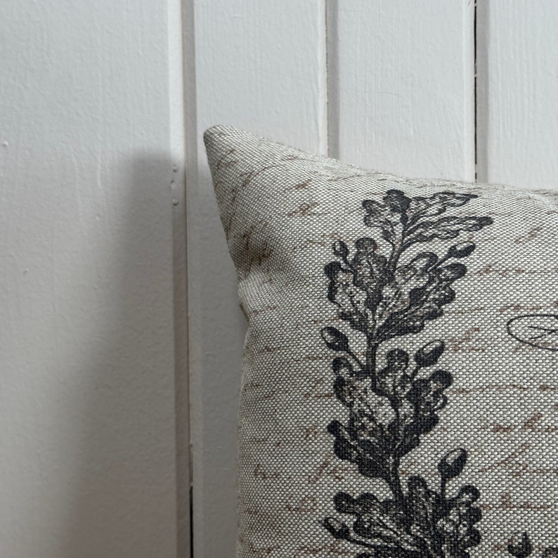 May include: A cream-colored pillow with a black floral design. The pillow has a textured fabric and a subtle sheen.