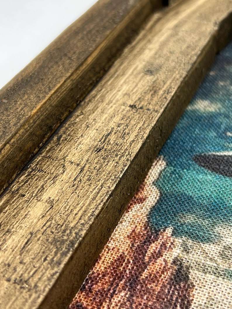 May include: Close-up of a wooden frame with a distressed, brown finish. The frame is partially covering a colorful fabric with a pattern of abstract shapes.