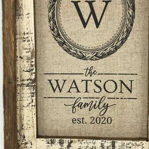 May include: A framed canvas print with a black and white floral design and the letter "W" in a circle. The text "the WATSON family est. 2020" is printed below the design.