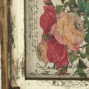 May include: A framed print with a floral design featuring pink and red roses. The print has a vintage aesthetic with a distressed white frame and a handwritten inscription that reads "La Minute Cast Pagnin".