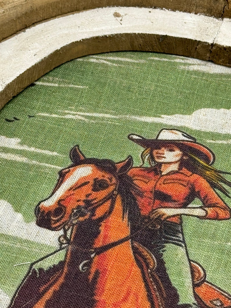 May include: A vintage-style illustration of a woman riding a brown horse. The woman is wearing a red shirt, a white cowboy hat, and blue jeans. The background is a green and white landscape.