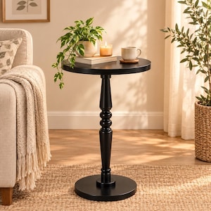 Peut inclure: Une table d'appoint ronde noire avec un plateau circulaire lisse et un pied central doté de détails tournés décoratifs. La table repose sur une base circulaire plate et présente une finition noire mate unie sur toute sa structure.