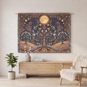 May include: A woven tapestry blanket featuring a dark blue background with a central tree of life motif, orange moon, and intricate floral patterns in shades of gold, orange, and blue. The rectangular textile has a fringed edge on all four sides.