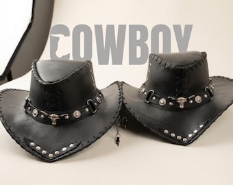 May include: Two black cowboy hats featuring silver-toned metal studs, a decorative band with a central bull skull emblem, and stitched edges. The word COWBOY is printed in large, bold, grey capital letters across the upper portion of the image.