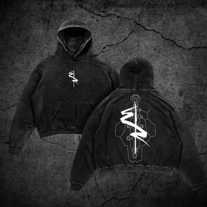 Op de afbeelding: Een zwarte hoodie met een wit grafisch logo op de borst en een groot wit geometrisch ontwerp op de achterkant. De trui heeft lange mouwen, een kangoeroezak aan de voorzijde en een vervaagde textuur in de stof.