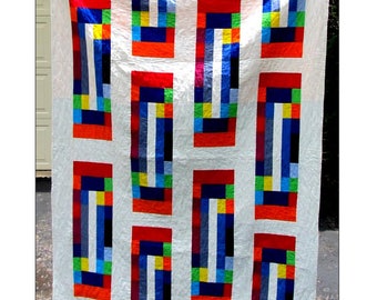 May include: A white quilt with a colorful geometric design. The quilt features rectangular blocks with red, blue, yellow, and green accents. The word "Fiesta" is in red at the top. The quilt is from Four Robbins Designs.