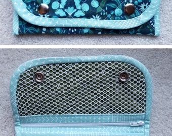 May include: A blue and green quilted fabric zippered pouch with a mesh pocket and snap closures. The pouch has a floral pattern and a light blue trim.