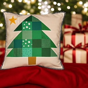 May include: Square cushion featuring a patchwork Christmas tree design. The tree is composed of green squares and triangles, with a yellow star. The cushion has a cream background and a black beaded trim around the edge.