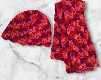 May include: A crocheted hat and scarf set in shades of pink, red, and purple. The hat is a slouchy beanie style and the scarf is a long, rectangular shape.
