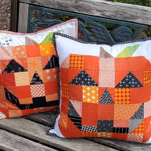 May include: Two square Halloween-themed throw pillows. Each pillow features a patchwork design of orange, black, white, and green fabrics, creating a jack-o'-lantern face. The pillows have white borders with decorative trim.