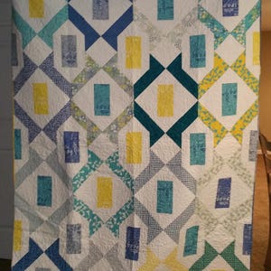 May include: A white quilt with a geometric pattern in shades of blue, yellow, green, and white. The quilt is made up of squares and diamonds.