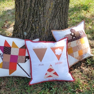 Könnte beinhalten: Drei dekorative Kissen mit Patchwork-Designs und weißen Hintergründen. Ein Kissen zeigt ein Sternmuster, ein anderes hat Tortenstückformen mit den Wörtern "pecan", "pumpkin" und "cherry", und das dritte hat eine Patchwork-Eichelform.