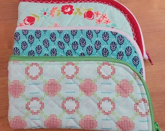 May include: Three quilted zippered pouches in various patterns. The top pouch has a floral pattern with red, white, and green accents. The middle pouch has a teal and white leaf pattern. The bottom pouch has a green and red geometric pattern.