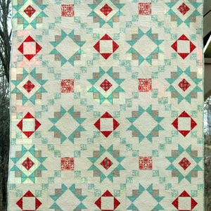 Peut inclure: Une courtepointe rectangulaire présentant un motif répétitif de blocs en forme d'étoile et de carrés. Le design intègre un fond crème avec des pointes d'étoiles bleu clair et grises, accentuées par des carrés à motifs floraux rouges.