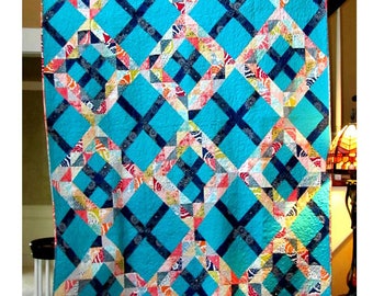 May include: A turquoise and navy blue quilt with a geometric pattern. The quilt is called "Crossing Waves" and is designed by Four Robbins Designs.
