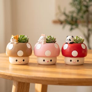 May include: Three mushroom-shaped ceramic planters with smiling faces. The left is brown with a cat, the center is pink with a rabbit, and the right is red with a panda. Each planter holds a small green succulent plant on top.