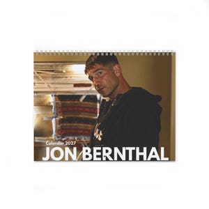 May include: A spiral-bound wall calendar for the year 2027 featuring a photographic portrait of actor Jon Bernthal. The image shows him in a dark hooded garment with a tactical vest, with the text Calendar 2027 JON BERNTHAL printed at the bottom.