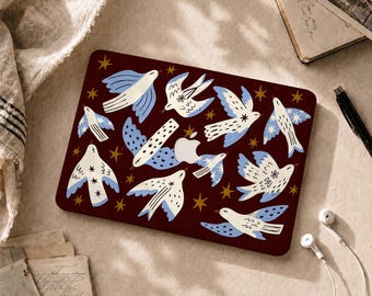 Könnte beinhalten: Eine dunkelrote Laptop-Hülle mit einem sich wiederholenden Muster aus stilisierten weißen und hellblauen Vögeln im Flug, durchsetzt mit kleinen goldenen Sternen. Das Design enthält einen zentralen Ausschnitt, der das silberne Apple-Logo freigibt.