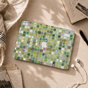 May include: A laptop skin featuring a mosaic pattern of small square tiles in various shades of green, light yellow, and iridescent white. The design covers the rectangular surface, centered around a silver Apple logo cutout on the device lid.
